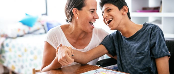 Mother and child sitting at a table smiling at one another.